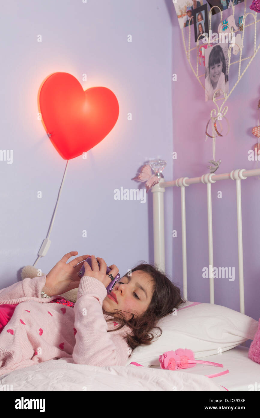 Adolescent girl playing games on her mobile phone in bed Stock Photo