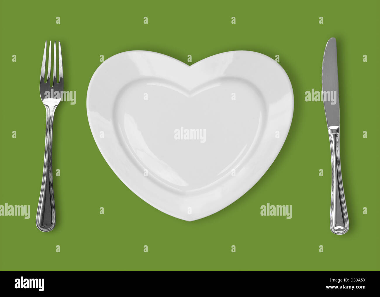 plate in shape of heart, table knife and fork on green background Stock Photo