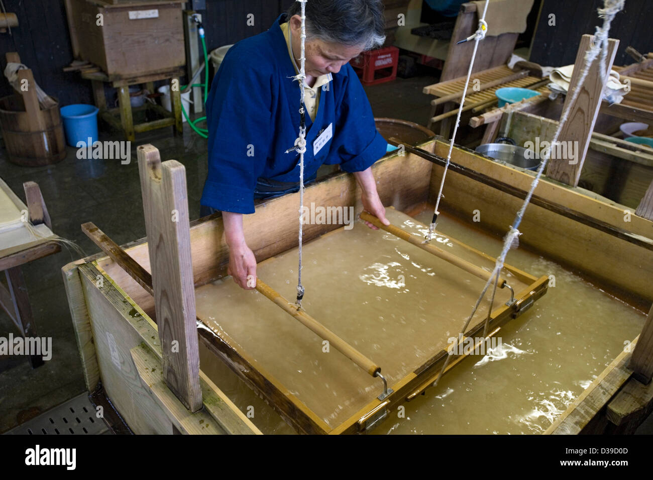Woman making traditional washi Japanese paper by hand in a wooden tub. Stock Photo