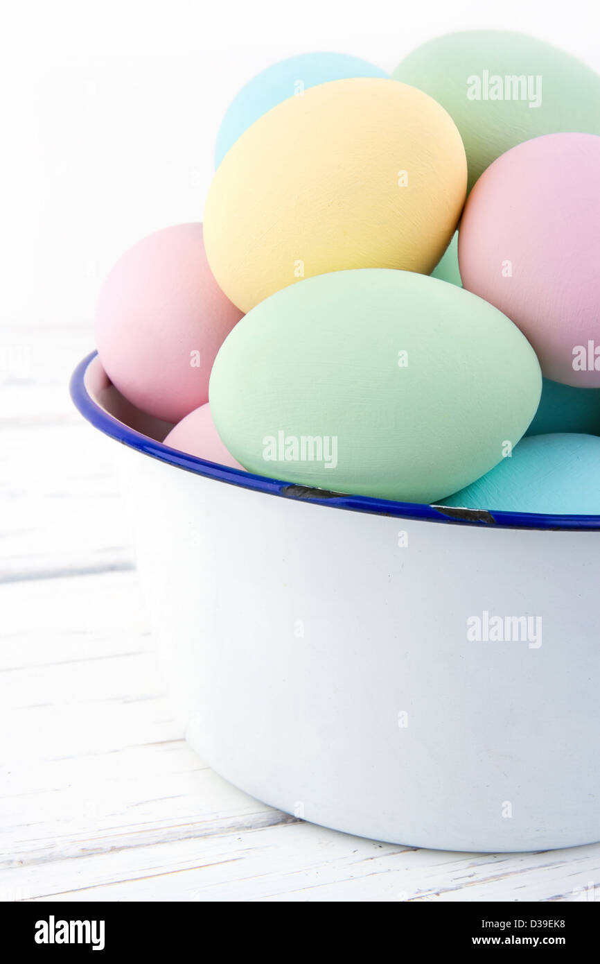 White old bowl full of pastel colored easter eggs on wooden background Stock Photo
