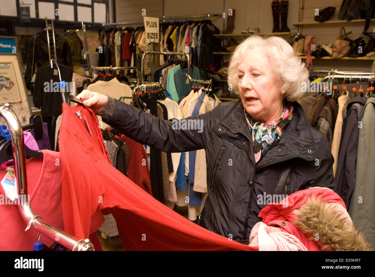 Elderly woman browsing clothing items on display in a charity shop, Godalming, Surrey, UK. Stock Photo