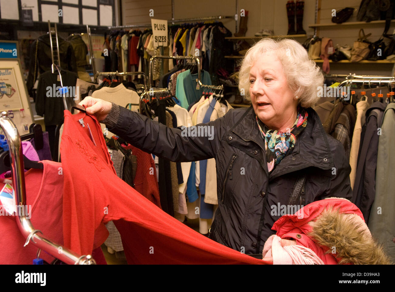 Elderly woman browsing clothing items on display in a charity shop, Godalming, Surrey, UK. Stock Photo