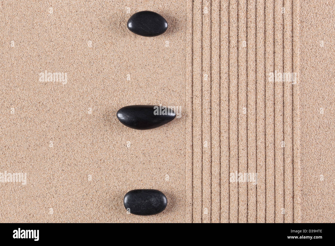 Three black pebbles on a raked sand zen garden. Stock Photo