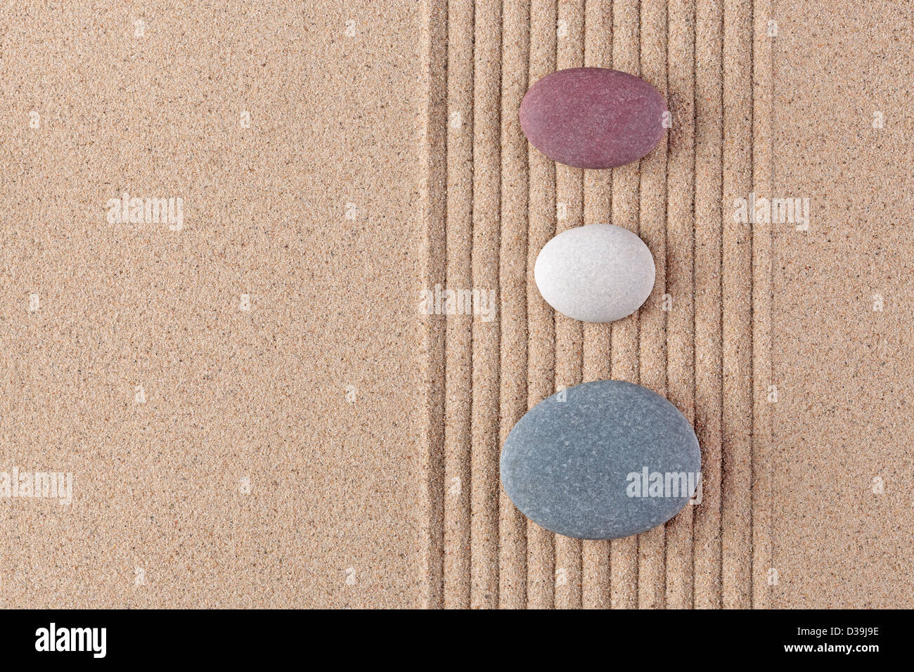 Three coloured pebbles on a raked sand zen garden. Stock Photo