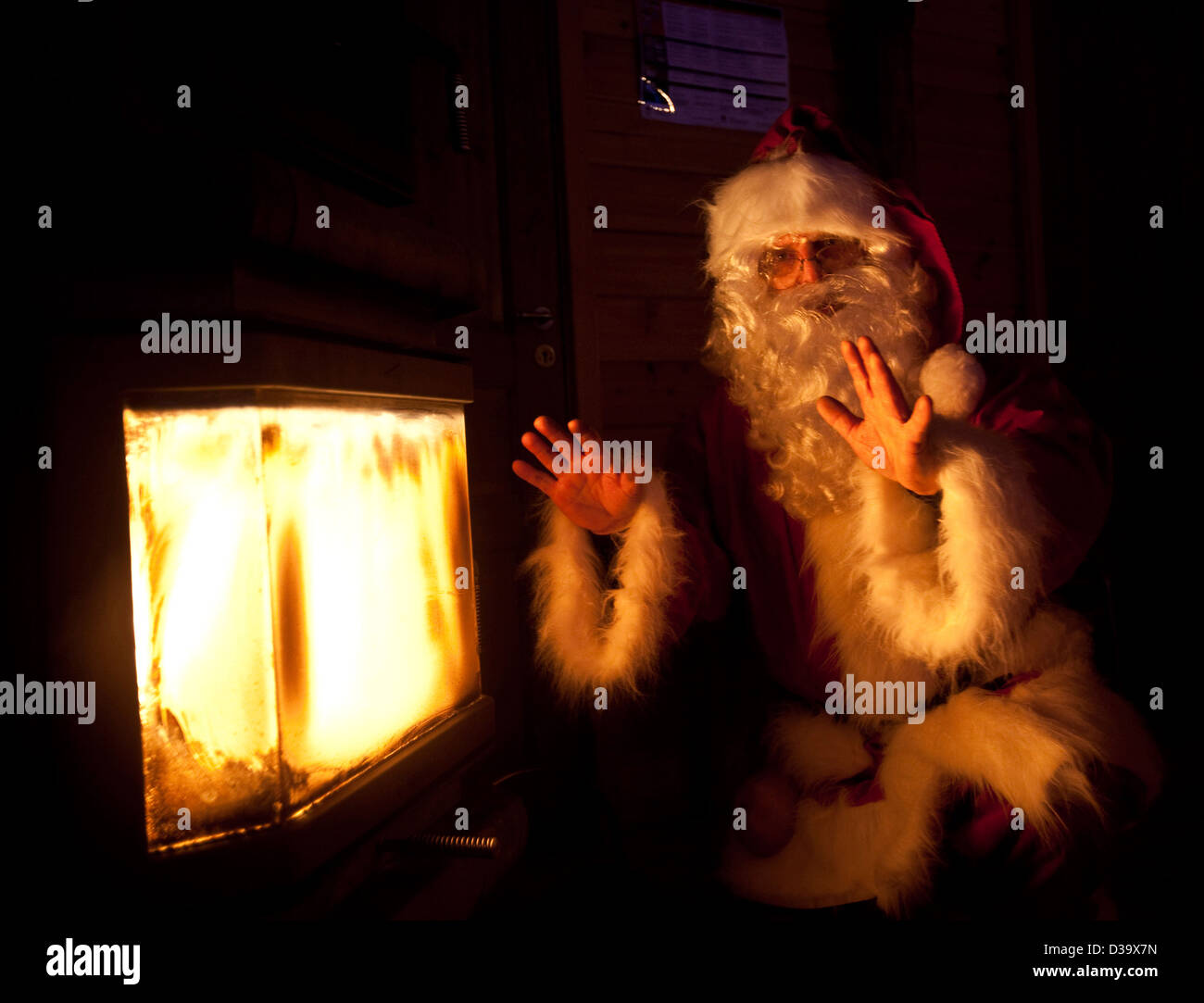 Man in father christmas costume warming hands by fire, Lapland Stock Photo