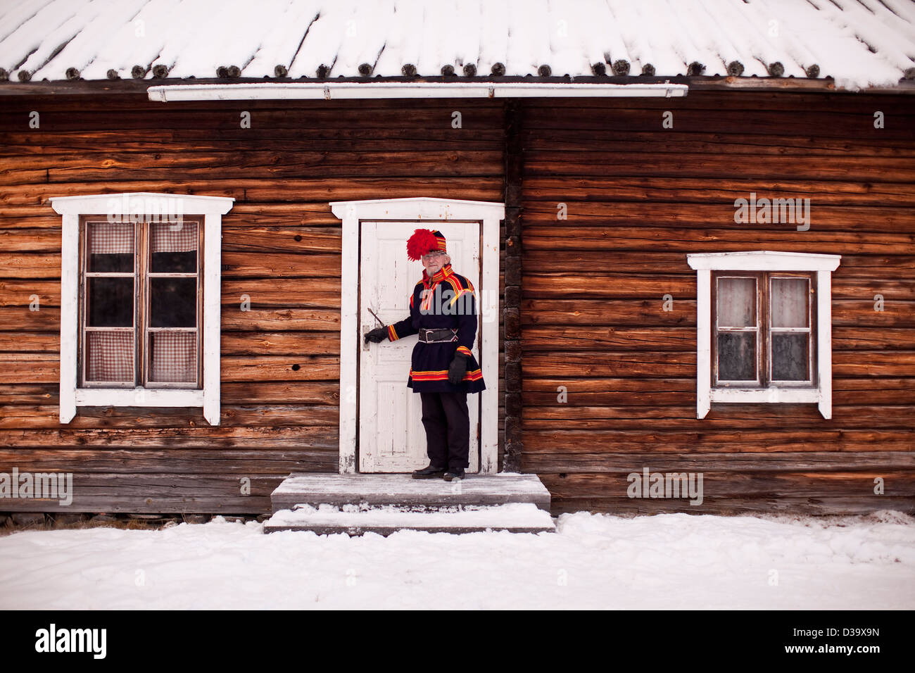 Man wearing traditional costume opening door to log cabin, Lapland Stock Photo