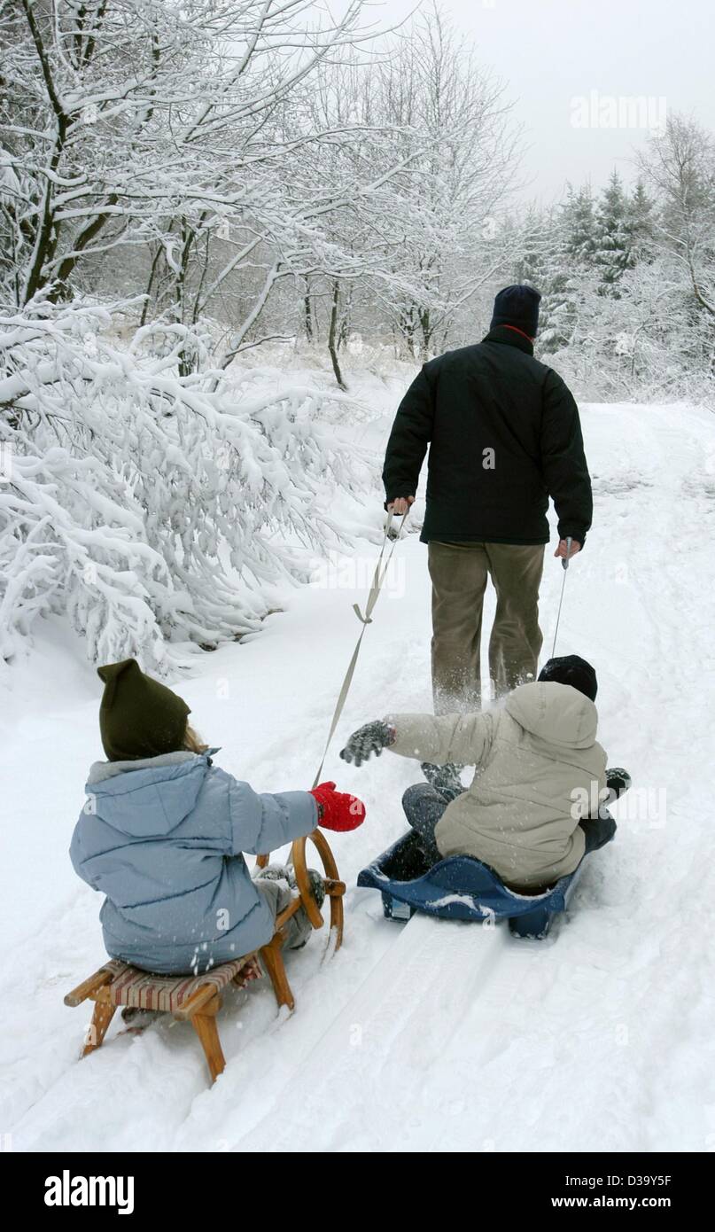 (dpa) - A father tows his two children on sleighs through the snow-covered landscape of the Hoher Meissner Mountain, Germany, 23 December 2003. Stock Photo