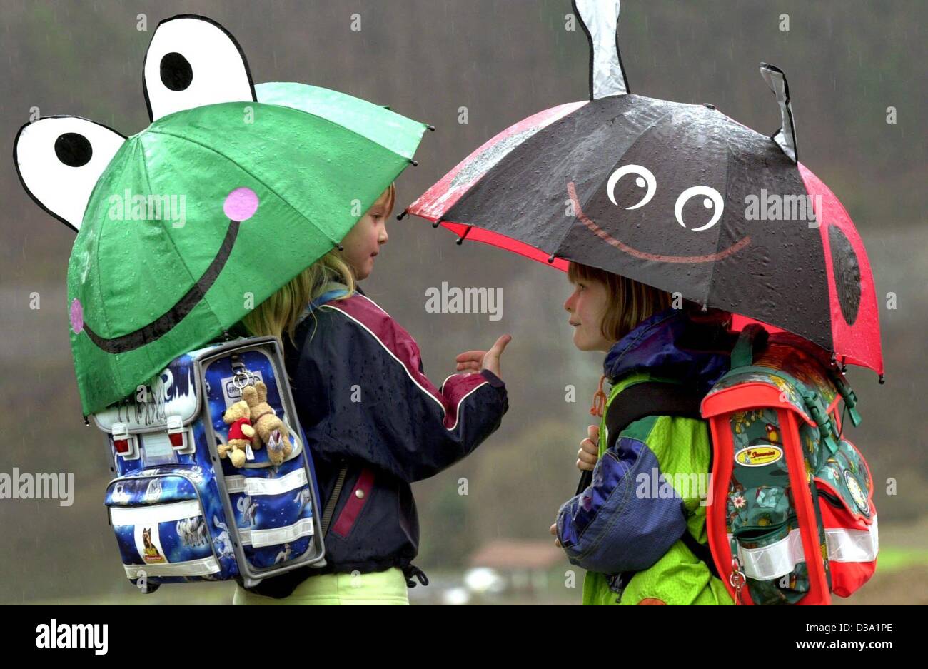 (dpa) - Two schoolgirls do not mind the rainy weather at all sheltered by their funny frog and beetle umbrellas on their way home in Edertal, mid Germany, 20 February 2002. Stock Photo