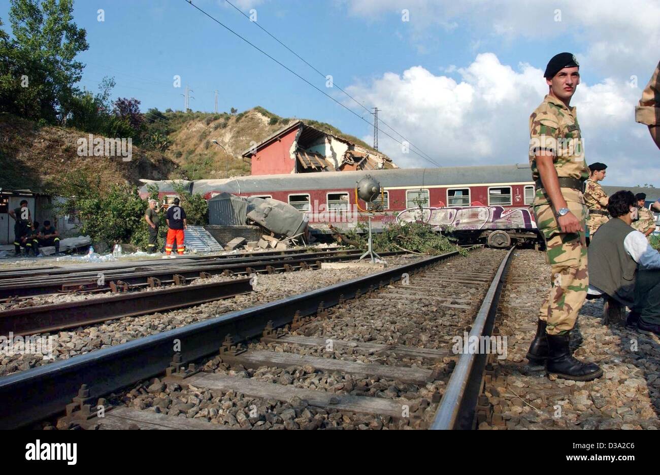 (dpa) - An Italian soldier stands in front of the derailed train in Rometta Marea, Italy, 21 July 2002. Eight people were killed and about 50 injured when the passenger train derailed in Sicily the day before. The train had left the Sicilian capital of Palermo and was approaching the north-eastern t Stock Photo