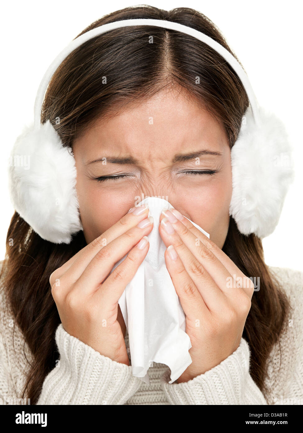 Sneezing woman sick blowing nose. Young woman being cold wearing earmuffs and sweater. Asian Caucasian female model Stock Photo