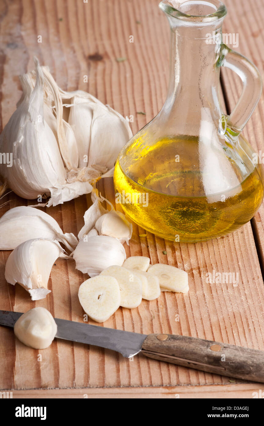 Chopped garlic, garlic cloves and virgin olive oil with a knife on a wooden board Stock Photo