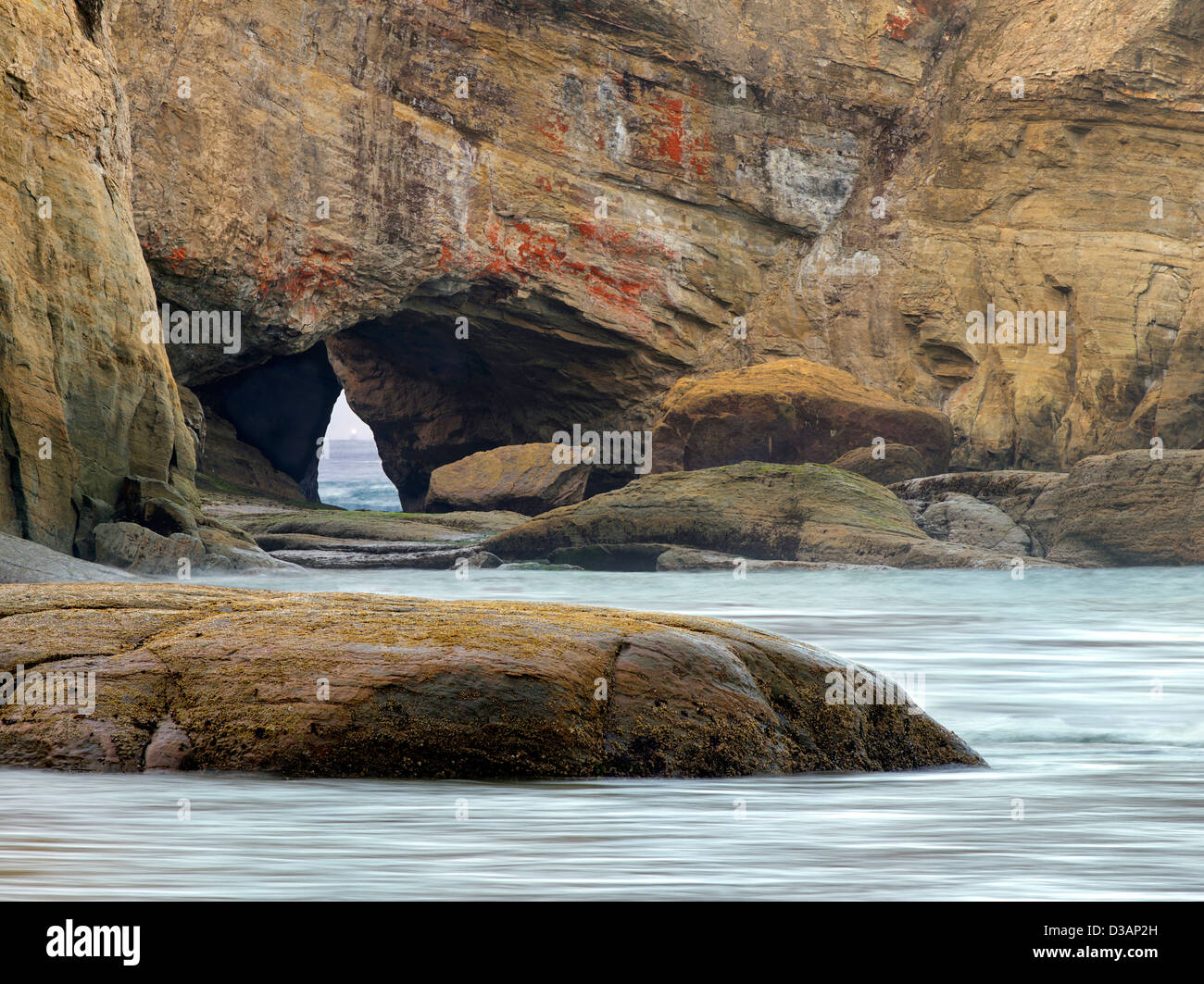 Beach with arch and light of boat in arch at Devil's Punchbowl State Natural Area. Oregon Stock Photo