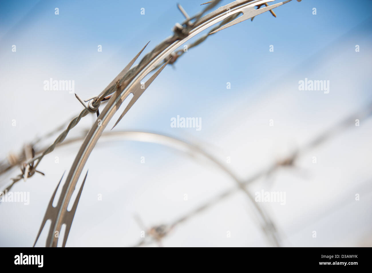 Coiled razor wire and barbed wire barrier against cloudy blue sky. Stock Photo