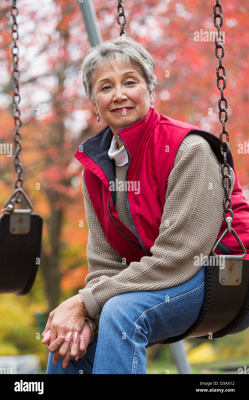 Mixed race woman on swing in park Stock Photo