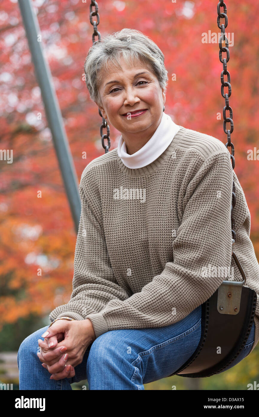 Mixed race woman on swing in park Stock Photo