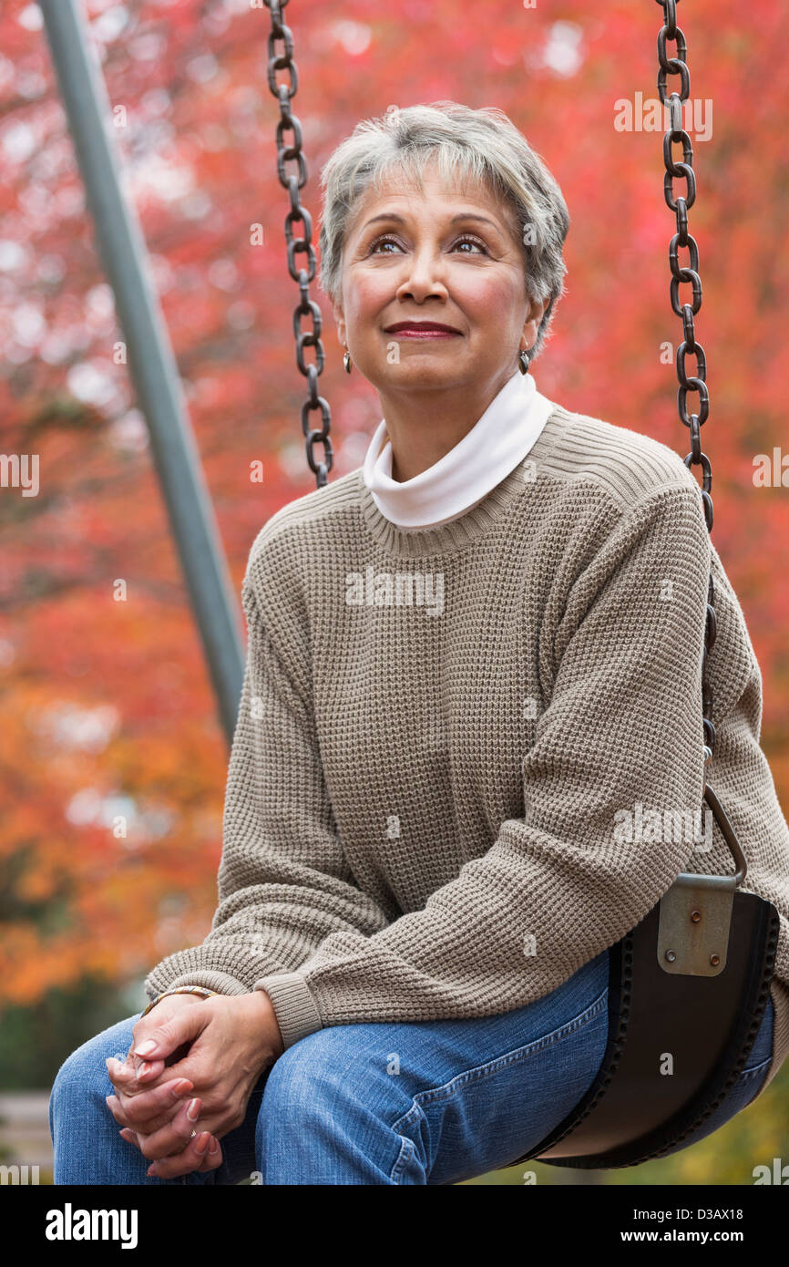 Mixed race woman on swing in park Stock Photo