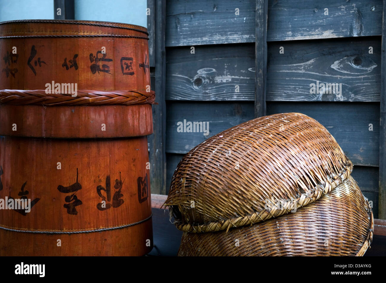 Simple composition of traditional Japanese containers including wooden barrels with kanji writing and woven bamboo baskets. Stock Photo