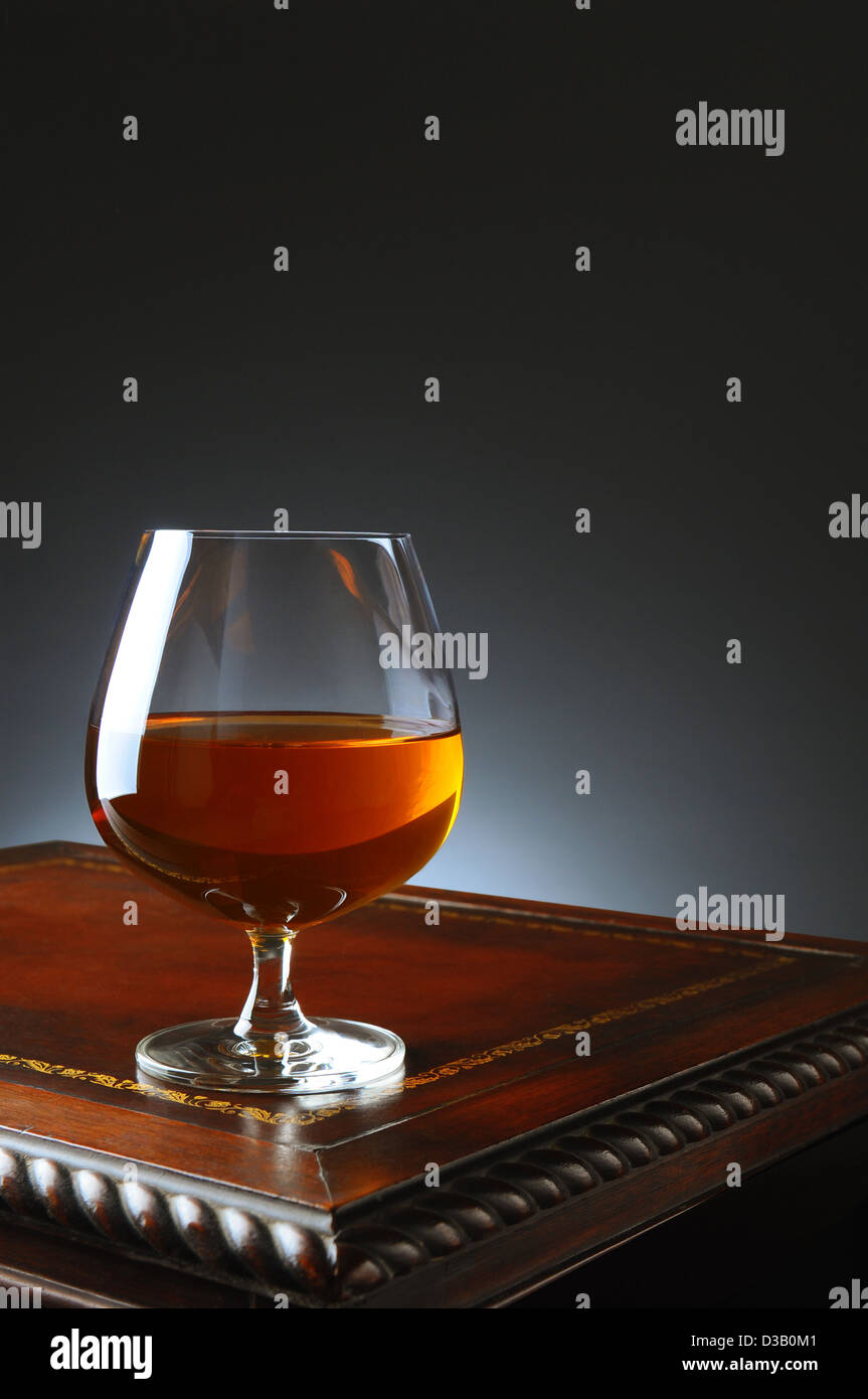 Closeup of a brandy snifter on a fancy antique wooden table with a light ot dark gray background. Stock Photo