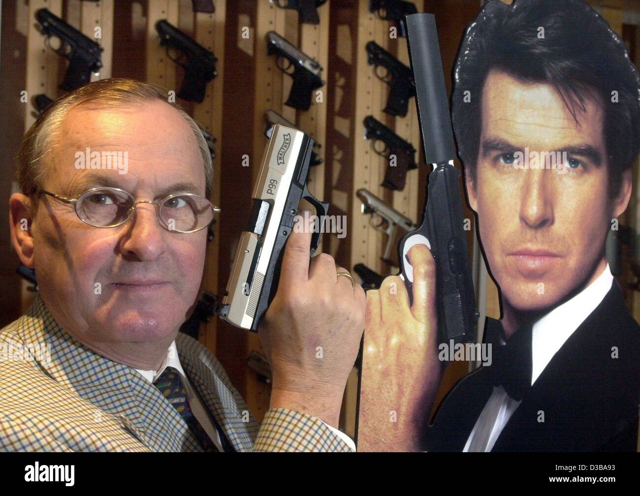 (dpa) - Fire arm producer Wulf-Heinz Pflaumer poses with the current James Bond weapon, a Walther P99, next to a cardboard model of 'James Bond' Pierce Brosnan, in the showroom of the Umarex gunsmith company in Arnsberg, Germany, 21 November 2002. Some 100,000 guns of the P99 model are produced annu Stock Photo