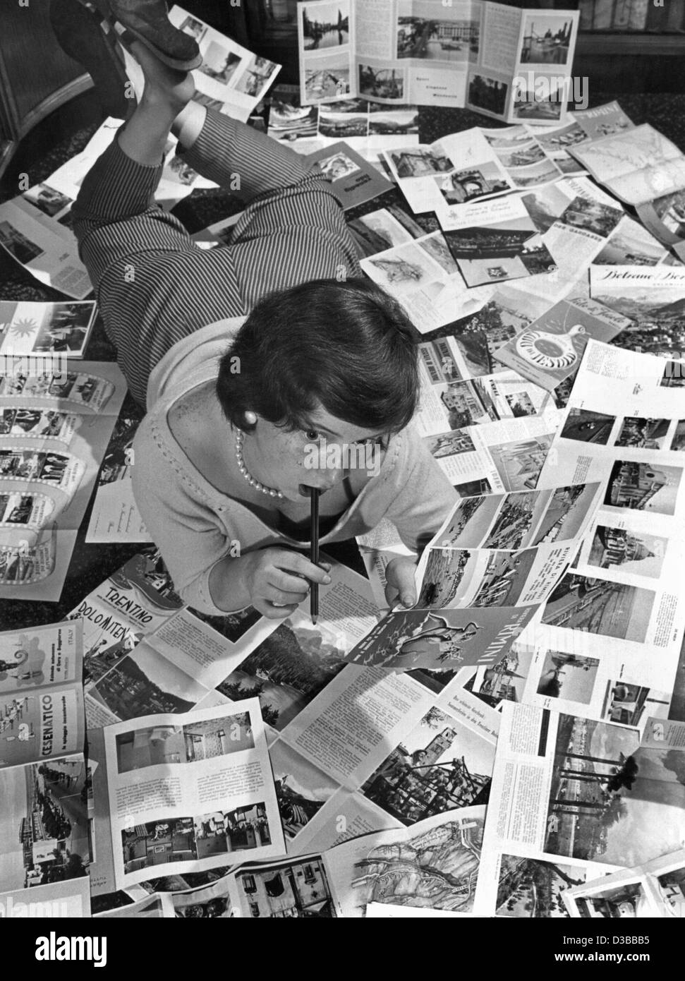 (dpa files) - A young woman studies travel brochures for the 1958 holiday travel season that are spread out around her in a photo taken in 1958.  According to the German travel agencies, holiday travel increased from the previous year. Stock Photo