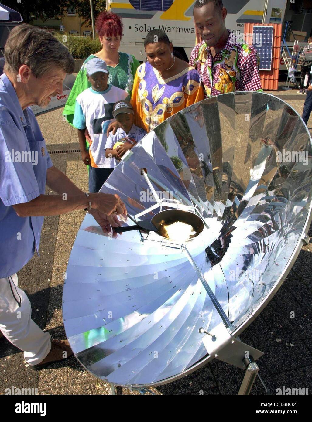 (dpa) - Dieter Zellweger (L) prepares a fried egg on a solar cooker on the Soltec trade fair in Hameln, Germany, 15 August 2002. A parabolic reflector in the shape of a satellite dish focuses the sunbeams on the frying pan. Rotary International and the German-Madagascan Club plan to introduce the so Stock Photo