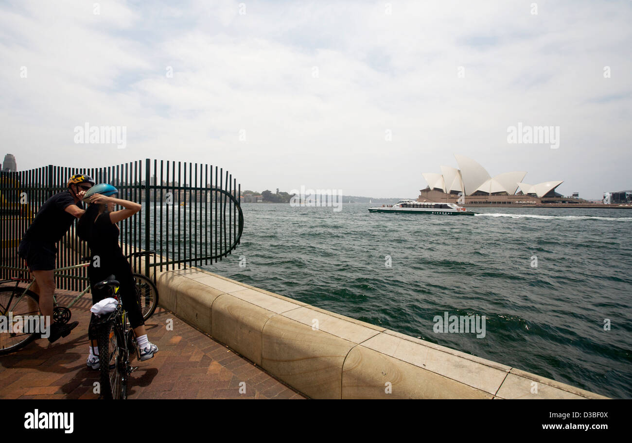 Two female cyclists stop and look from Circular Quay to the Sydney Opera House in Australia Stock Photo