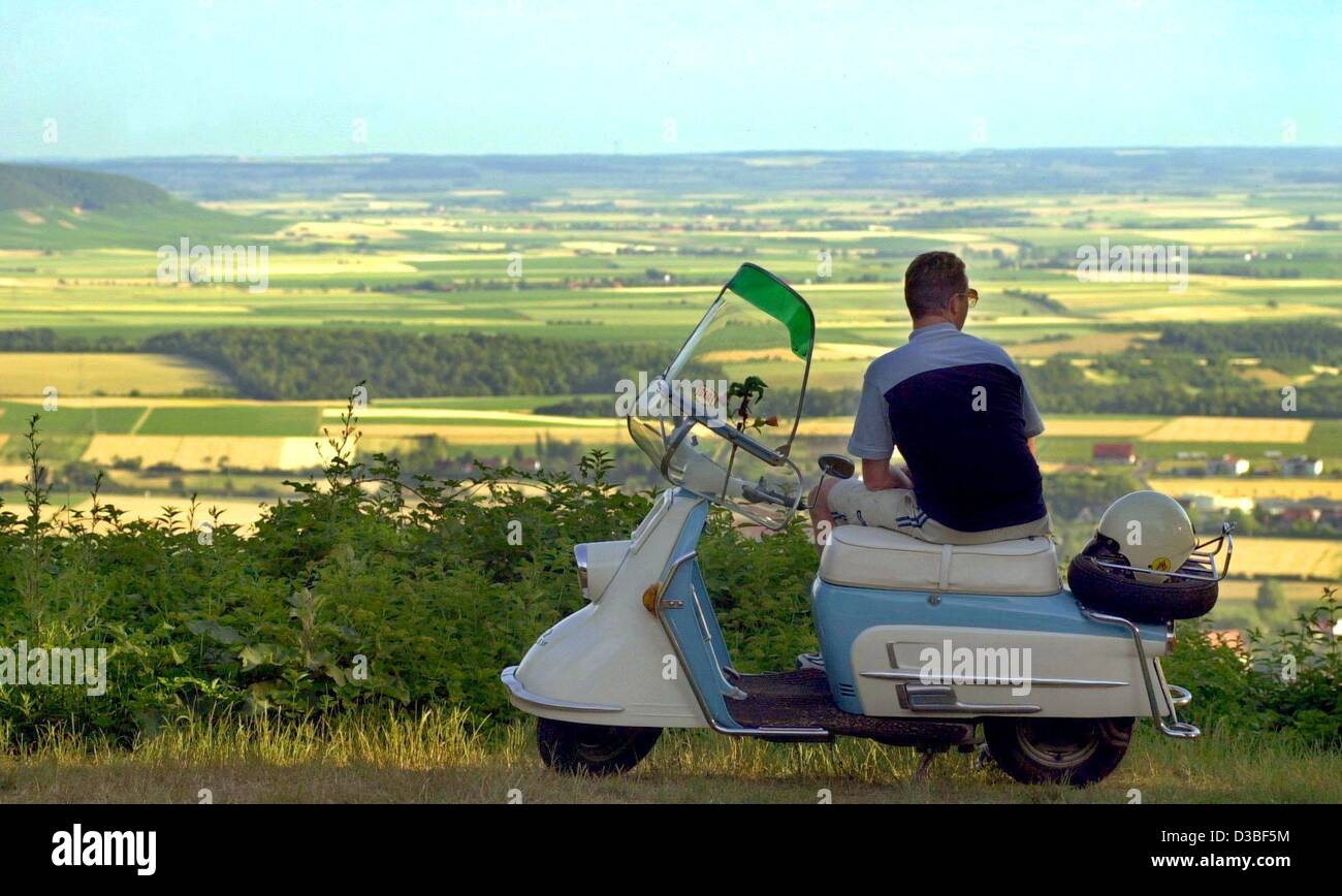 (dpa) - A jung man sits on his 43-year-old scooter of the type Heinkel and enjoys the panormaic view of the landscape at Iphofen, Germany, 26 June 2003. Stock Photo