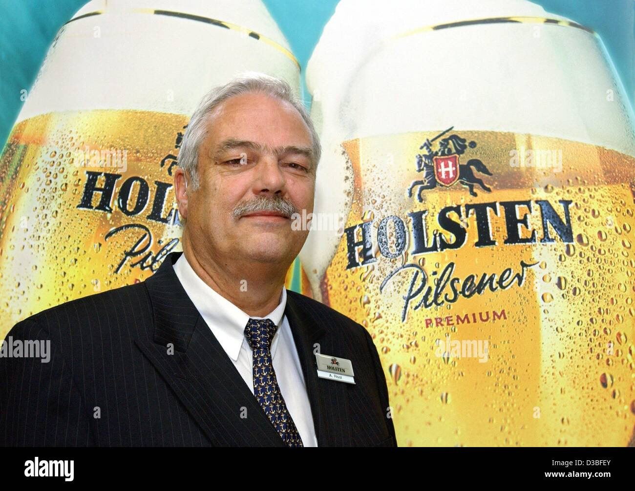 (dpa) - Andreas Rost, CEO of Holsten Brewery, is posing in front of a poster with two large Holsten beer glasses at the AGM in Hamburg, Germany, 18 June 2003. Rost said the drink can deposit has to be cancelled as it kills jobs. A new solution should be found in cooperation with drink producers, ret Stock Photo