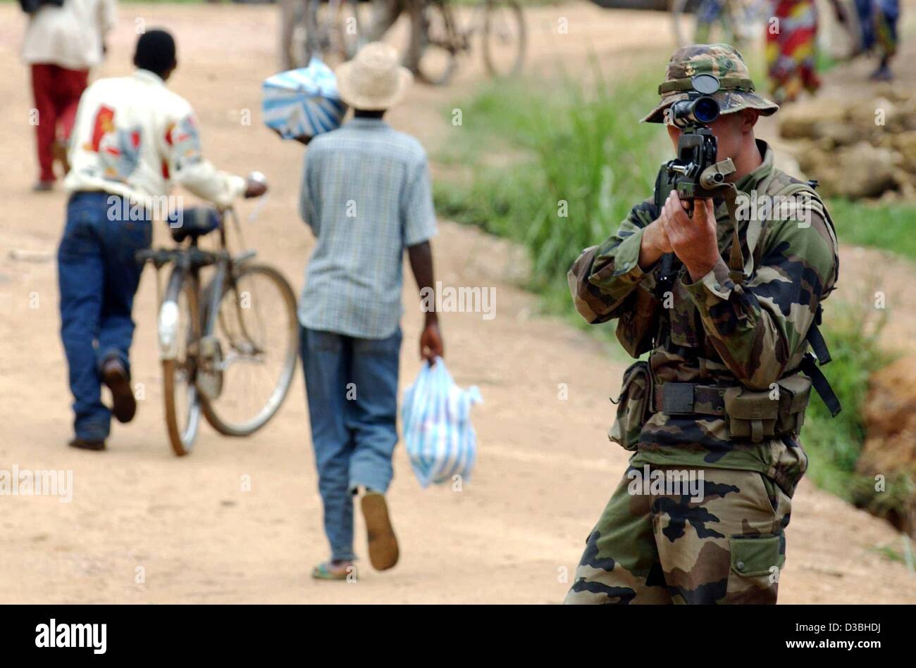 (dpa) - Congolese civilians walk past a French soldier who is aiming with his rifle at a checkpoint of the French army in Bunia, Democratic Republic of Congo, 11 June 2003. Meanwhile, more soldiers arrived for the French lead international task force. The task force is meant to prevent any further b Stock Photo