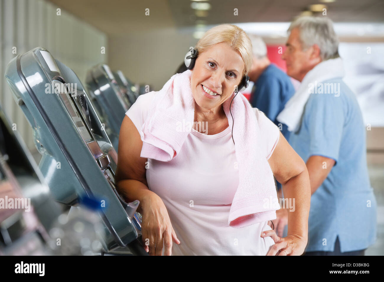 Happy senior woman with headphones on treadmill in gym Stock Photo