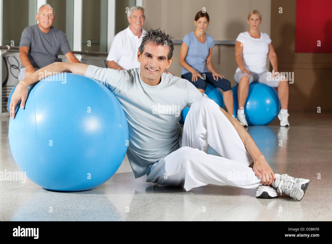 Happy man sitting with blue gym ball in fitness center with senior group Stock Photo
