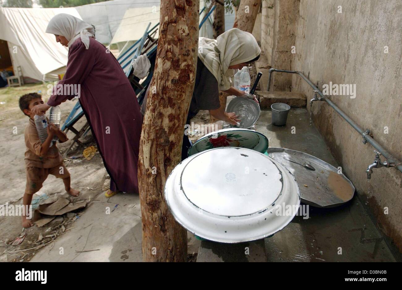 (dpa) - Palestinian women wash the dishes in a tent camp set up for families evicted from their homes, outside Baghdad, 22 May 2003. When U.S. forces seized the capital, the elite of Saddam Hussein's regime fled. Now, with no legal system left to stop them, families are flooding the buildings that w Stock Photo
