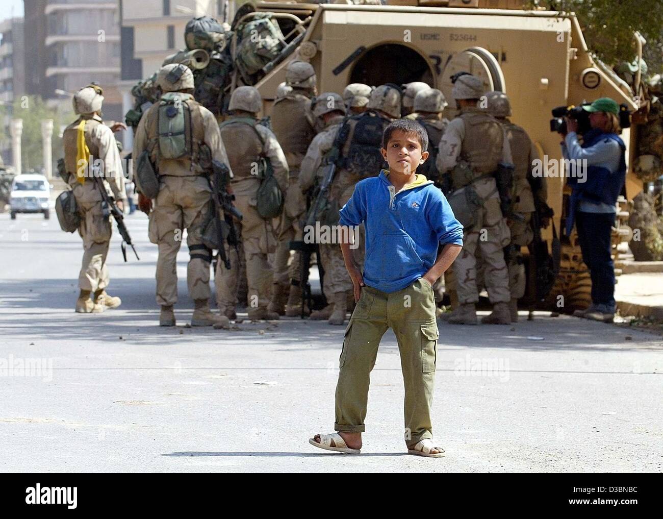 (dpa) - An Iraqi boys stands in front of a group of US soldiers in Iraq, 11 April 2003. The entire medical care in Baghdad has broken down, Red Cross officials said. Hospitals and clinics in the Iraqi capital are closed, the patients have either fled or are left on their own. The rising temperature  Stock Photo