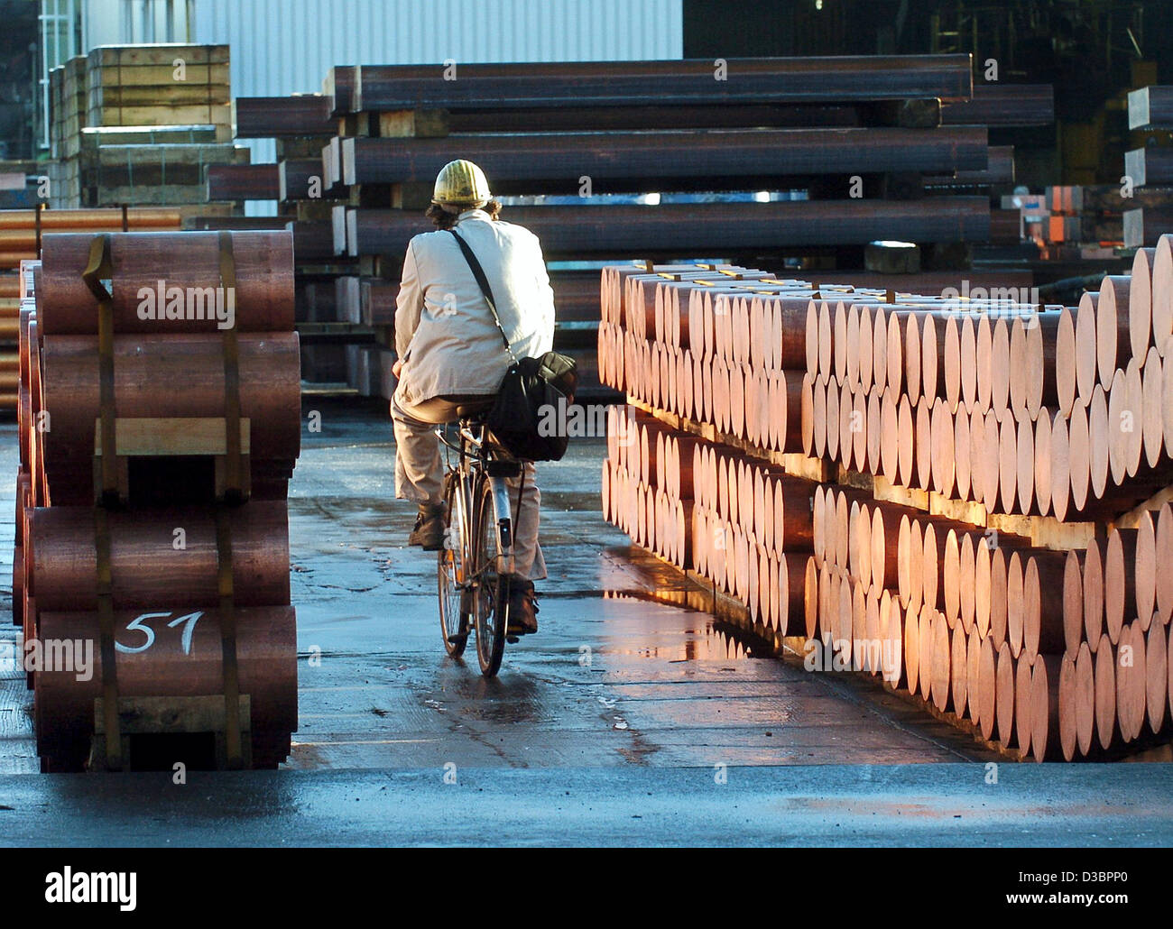 (dpa) - An employee of the Norddeutsche Affinerie (NA) cycles past poles of recycled copper in Hamburg, Germany, 29 December 2004. Due to the global hunger for raw materials metal recycling in Europe is increasing. As a result the Norddeutsche Affinerie (NA) is expanding its production capacities fo Stock Photo