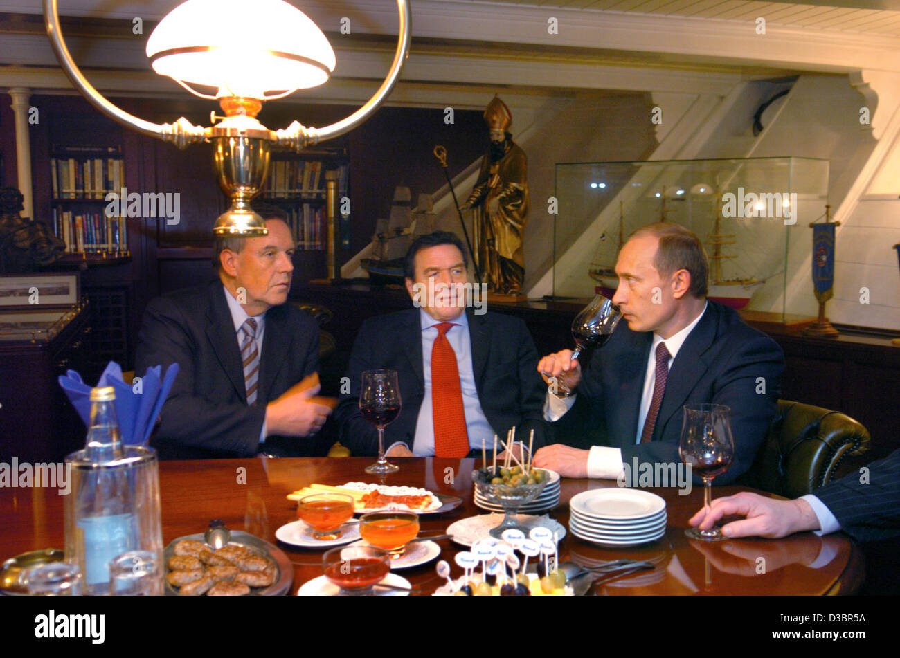 (dpa) - Russian President Vladimir Putin (R), German Chancellor Gerhard Schroeder (C) and Hamburg's politician Volker Ruehe (L) drink some wine at the captain's table of the museum ship 'Rickmer Rickmers' lying at anchor in the port in Hamburg, Monday 20 December 2004. Putin is on a two-day visit to Stock Photo