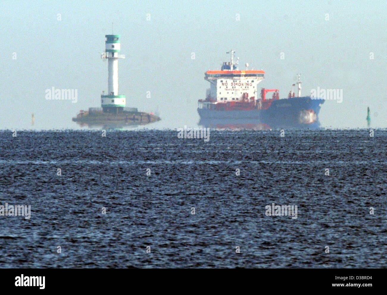(dpa) - A cargo ship passes by a lighthouse in the distance inlet to the Kieler Foerde (fjord) near Kiel, Germany, 1 October 2003. The lighthouse appears to hover above the water surface due to the mirage on the calm water. Stock Photo