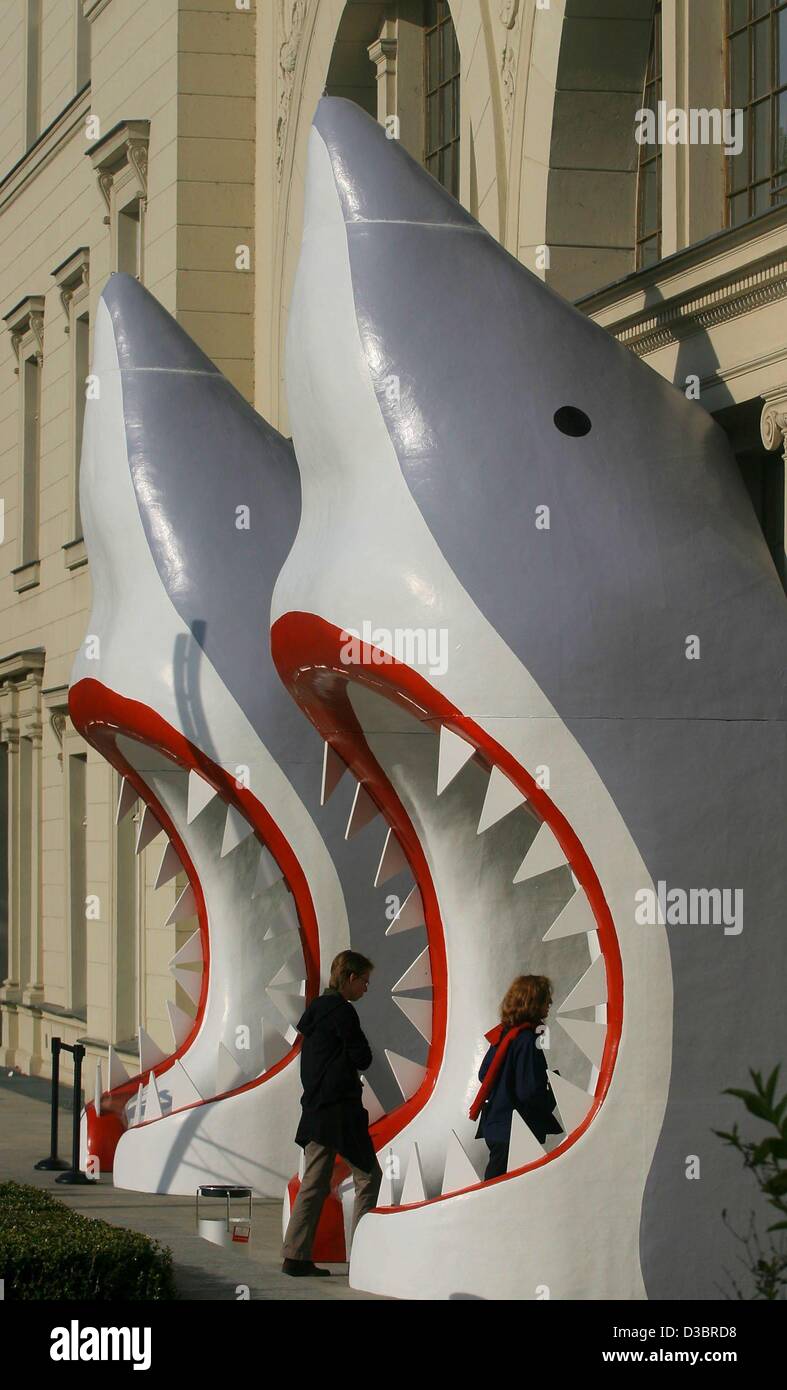 (dpa) - Two visitors walk through two six metres tall sculpturs which resemble the open jaws of sharks at the entrance of the National Gallery in Berlin, 1 October 2003. The sculptures are made from steel, styrofoam and fibreglass by the Australian artist Callum Morton. They are part of an exhibitio Stock Photo