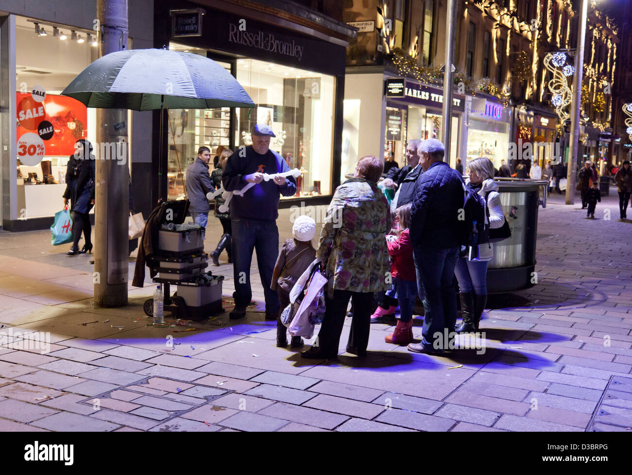 A group of people, adults and children, watch a balloon sculptor in Buchanan Street, in central Glasgow Stock Photo