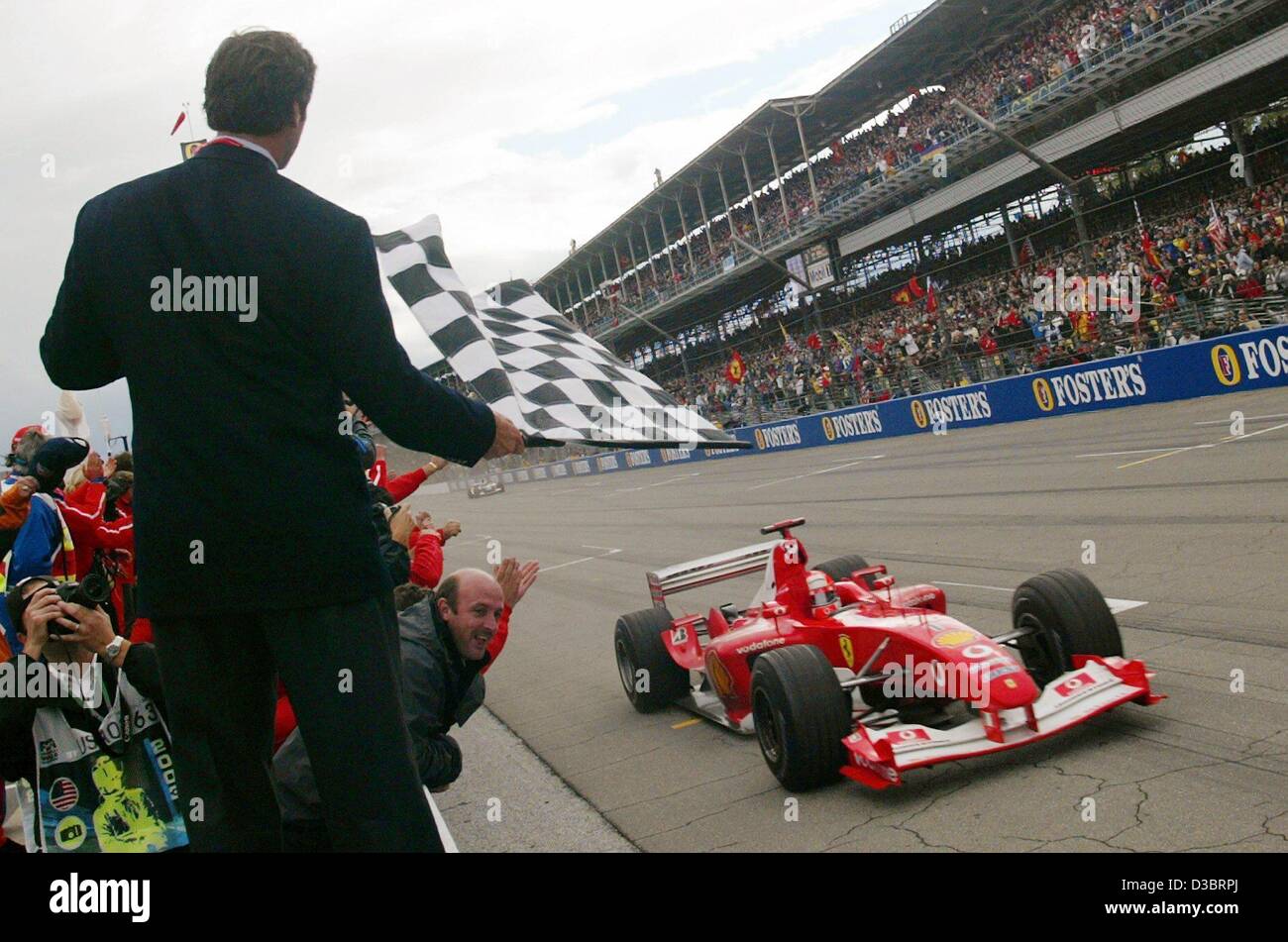 (dpa) - German formula one pilot and world champion Michael Schumacher (Ferrari) drives in his racing car on the racetrack past a tribune with cheering spectators as he is the first to arrive at the finishing line during the formula one US grand Prix in Indianapolis, USA, 28 September 2003. Schumach Stock Photo