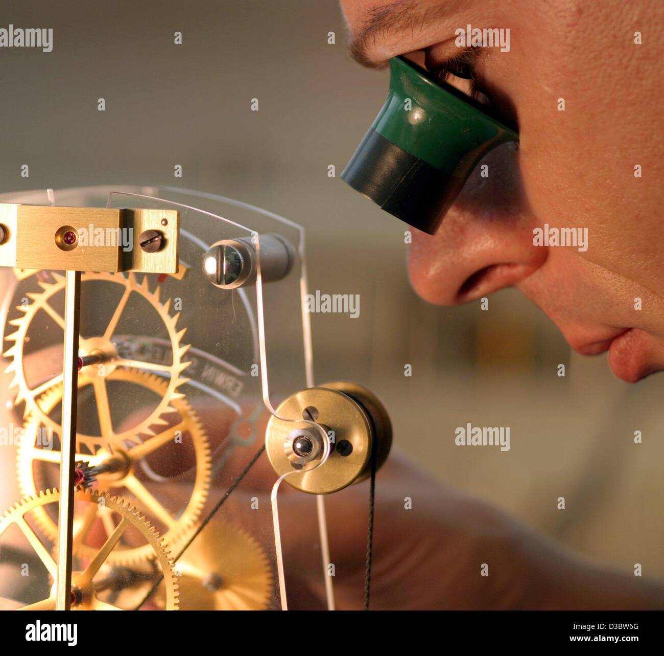 (dpa) A clockmaker studies the clockwork of one of his clocks at the