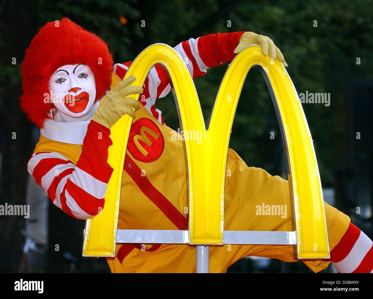 (dpa) - 'Ronald McDonald' poses behind the logo of the fast food chain McDonald's during a press conference in Munich, 2 September 2003. The slogan 'ich liebe es' ('i'm lovin' it') will soon make its way into the vocabulary of McDonald's customers in more than 100 countries as the Golden Arches laun Stock Photo