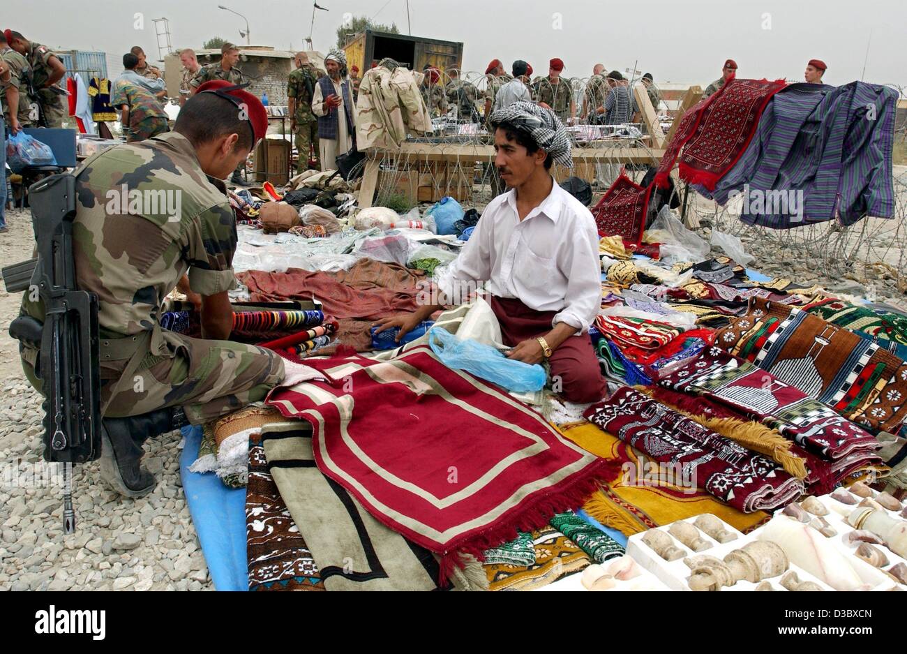 (dpa) - A German soldier looks, in his spare time, through stacks of carpets, textiles and other merchandise at the stand of a street trader in Kabul, Afghanistan, 3 August 2003. Germany continues to participate with more than 1,500 soldiers in the International Securtiy Assistance Force (ISAF) whic Stock Photo