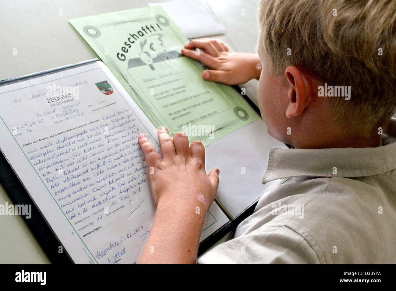 (dpa) - A first grader looks at his first end-of-year school report ('Zeugnis') at an elementary school in Magdeburg, Germany, 9 July 2003. The headline of the green paper reads 'Geschafft!' (made it!). The day was also the last day of school before the start of the summer holidays. Stock Photo
