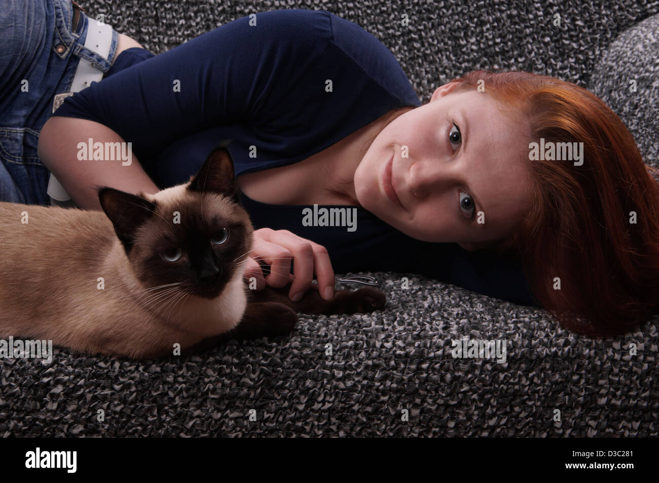young woman and siamese cat lazing on couch Stock Photo