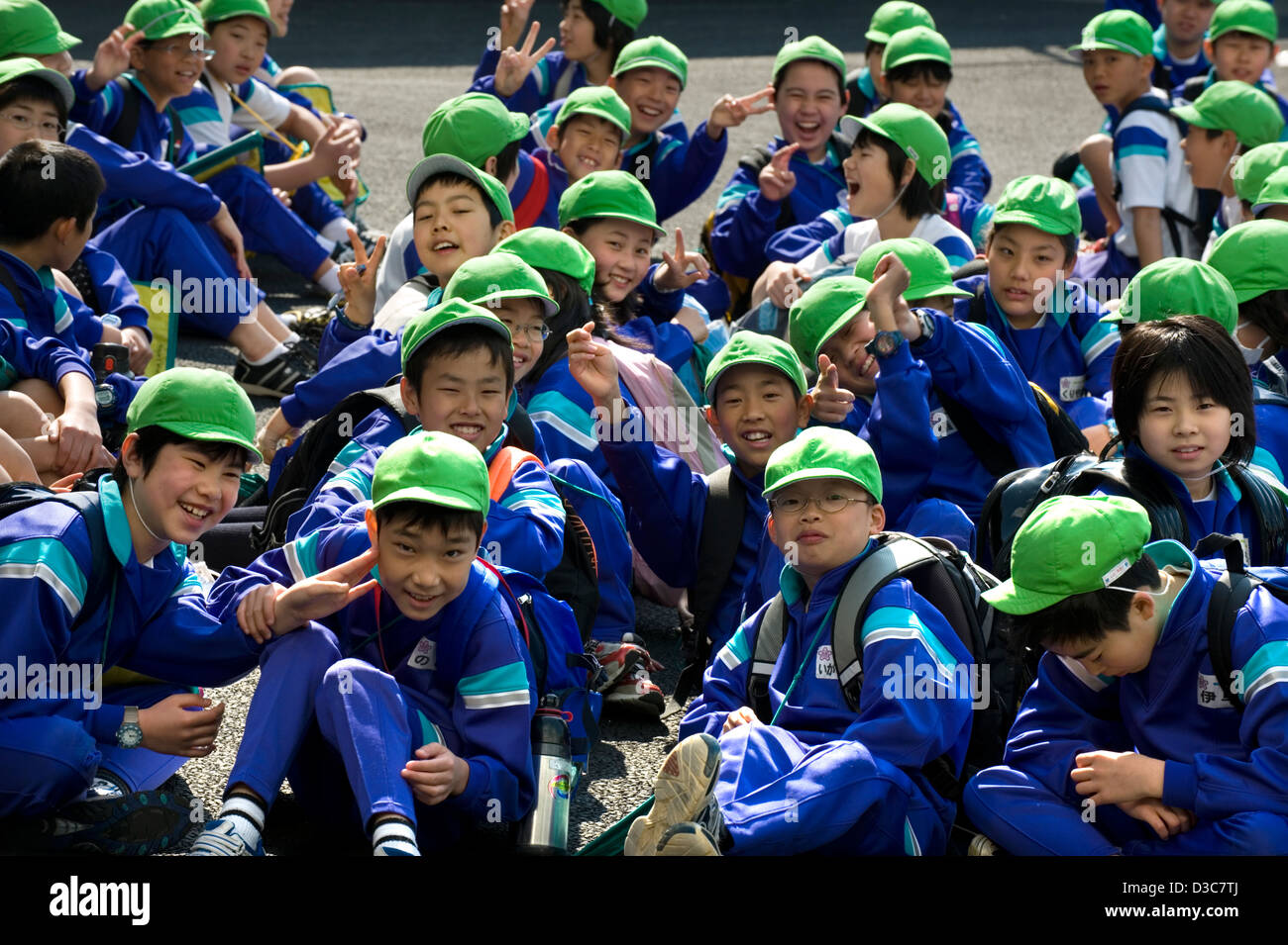 Smiling happy faces of Japanese elementary school boys and girls wearing colorful green caps and flashing the peace sign. Stock Photo