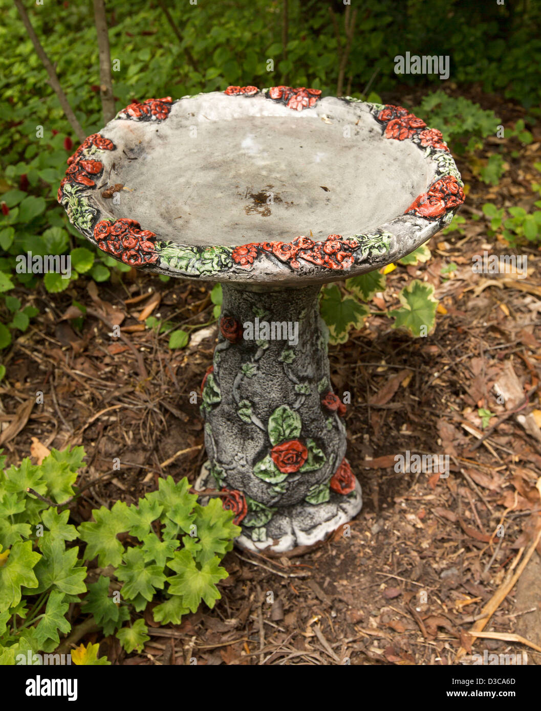 Unique and ornate bird bath decorated with red roses and green leaves in a garden setting Stock Photo