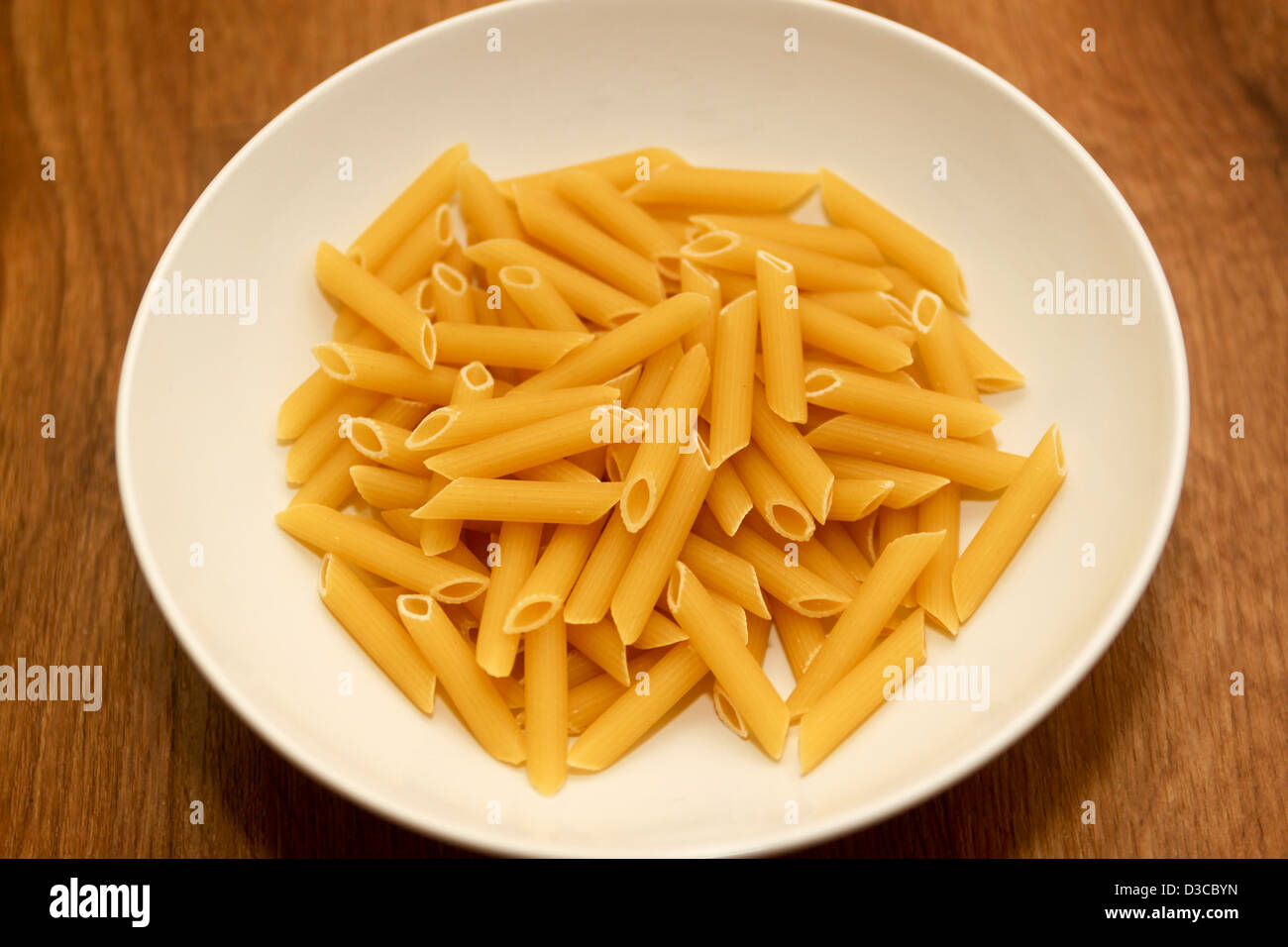 Dry uncooked penne pasta in white bowl Stock Photo