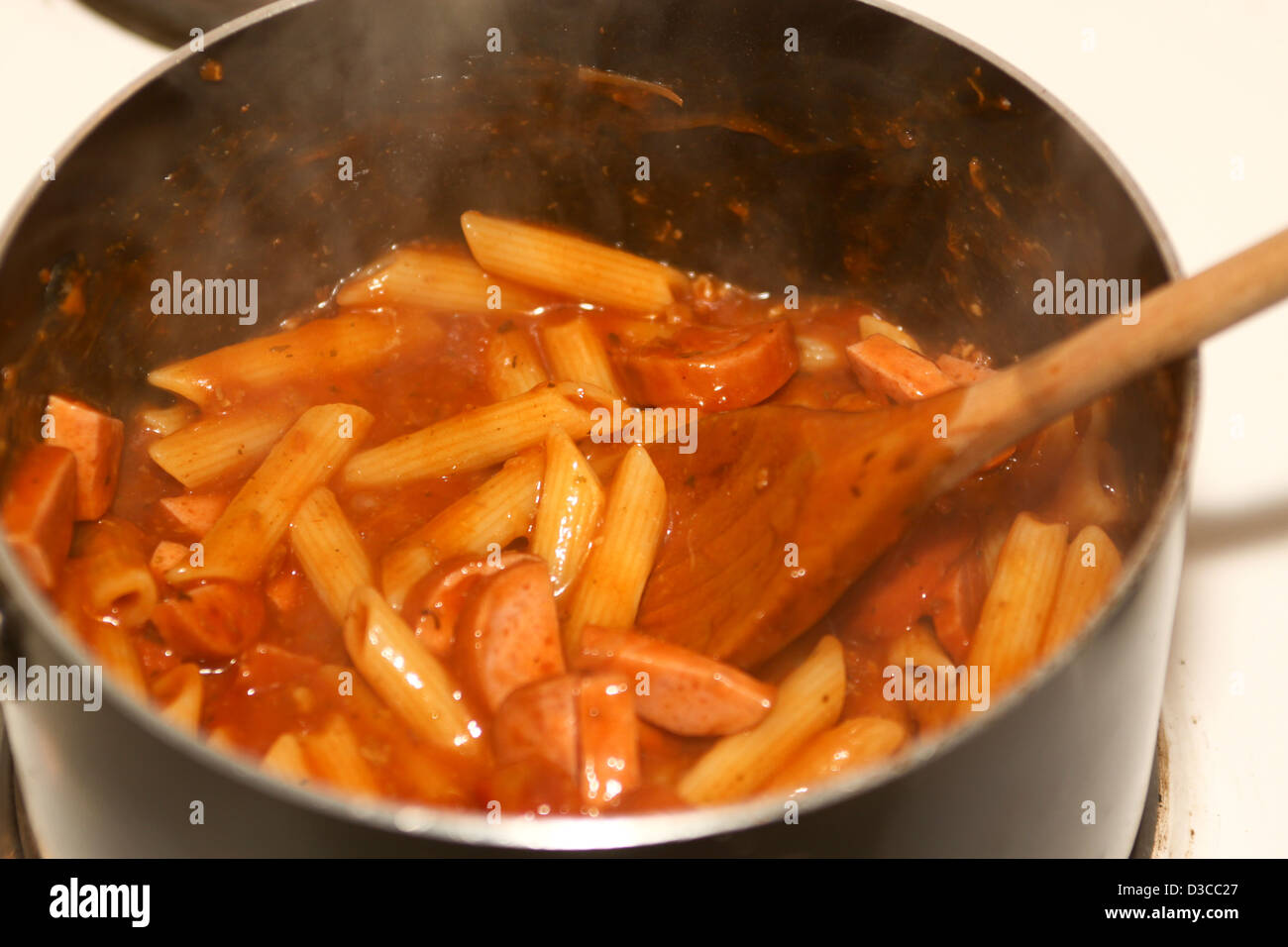 Penne pasta in pan with sauce and sliced smoked spicy sausage Stock Photo