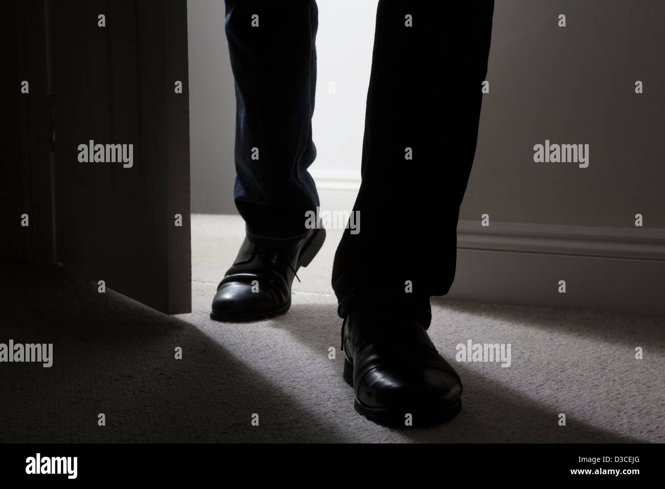 Close up of adult male legs and feet wearing black shoes entering a dark room. Silhouette. Stock Photo