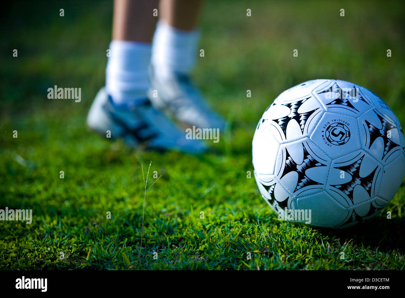 Image of close up football on green playing field person warming up in background Stock Photo